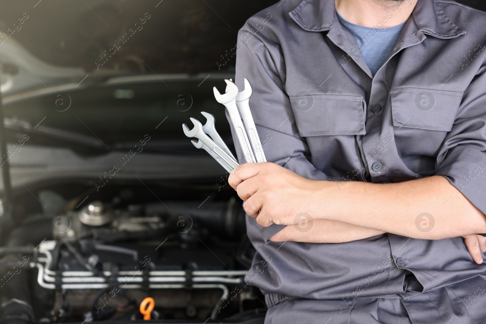 Auto parts. Professional mechanic with different wrenches near open hood of car indoors, closeup. Space for text Photo of Auto parts. Professional mechanic with different wrenches near open hood of car indoors, closeup. Space for text