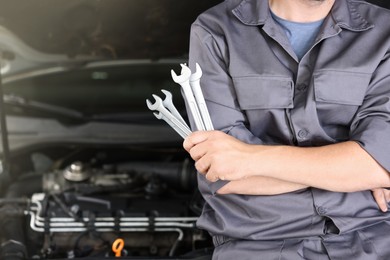 Photo of Auto parts. Professional mechanic with different wrenches near open hood of car indoors, closeup. Space for text