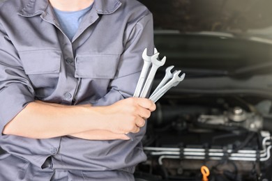 Photo of Auto parts. Professional mechanic with different wrenches near open hood of car indoors, closeup. Space for text
