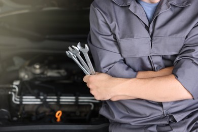 Photo of Auto parts. Professional mechanic with different wrenches near open hood of car indoors, closeup. Space for text