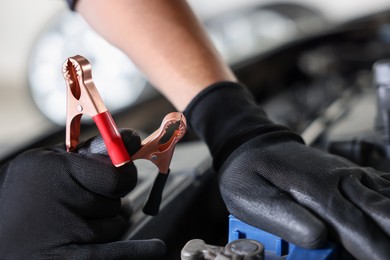 Photo of Auto part. Professional mechanic with crocodile clip near open hood of car indoors, closeup