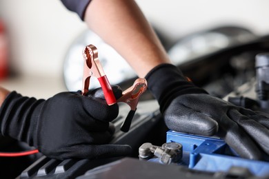Photo of Auto part. Professional mechanic with crocodile clip near open hood of car indoors, closeup