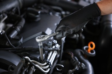 Photo of Auto parts. Professional mechanic with torque wrench fixing car indoors, closeup