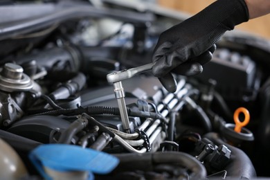 Photo of Auto parts. Professional mechanic with torque wrench fixing car indoors, closeup