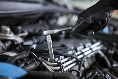 Photo of Auto parts. Professional mechanic with torque wrench fixing car indoors, closeup