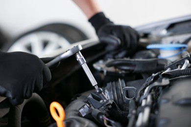 Photo of Auto parts. Professional mechanic with torque wrench fixing car indoors, closeup