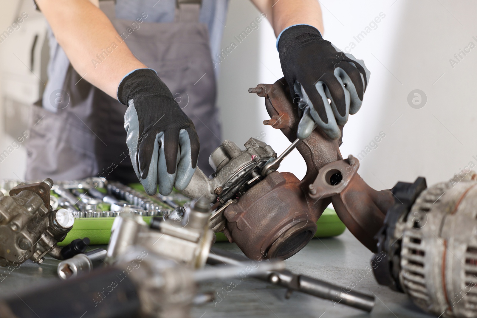 Auto parts. Professional mechanic with wrench fixing turbocharger at table indoors, closeup Photo of Auto parts. Professional mechanic with wrench fixing turbocharger at table indoors, closeup