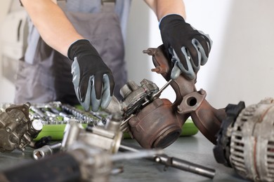 Photo of Auto parts. Professional mechanic with wrench fixing turbocharger at table indoors, closeup