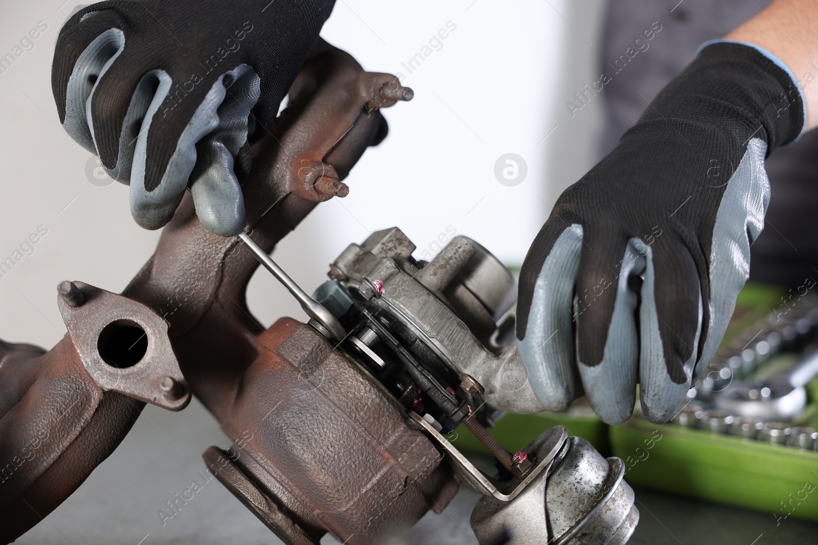 Auto parts. Professional mechanic with wrench fixing turbocharger at table indoors, closeup Photo of Auto parts. Professional mechanic with wrench fixing turbocharger at table indoors, closeup