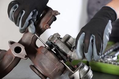 Photo of Auto parts. Professional mechanic with wrench fixing turbocharger at table indoors, closeup