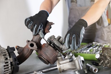 Photo of Auto parts. Professional mechanic with wrench fixing turbocharger at table indoors, closeup