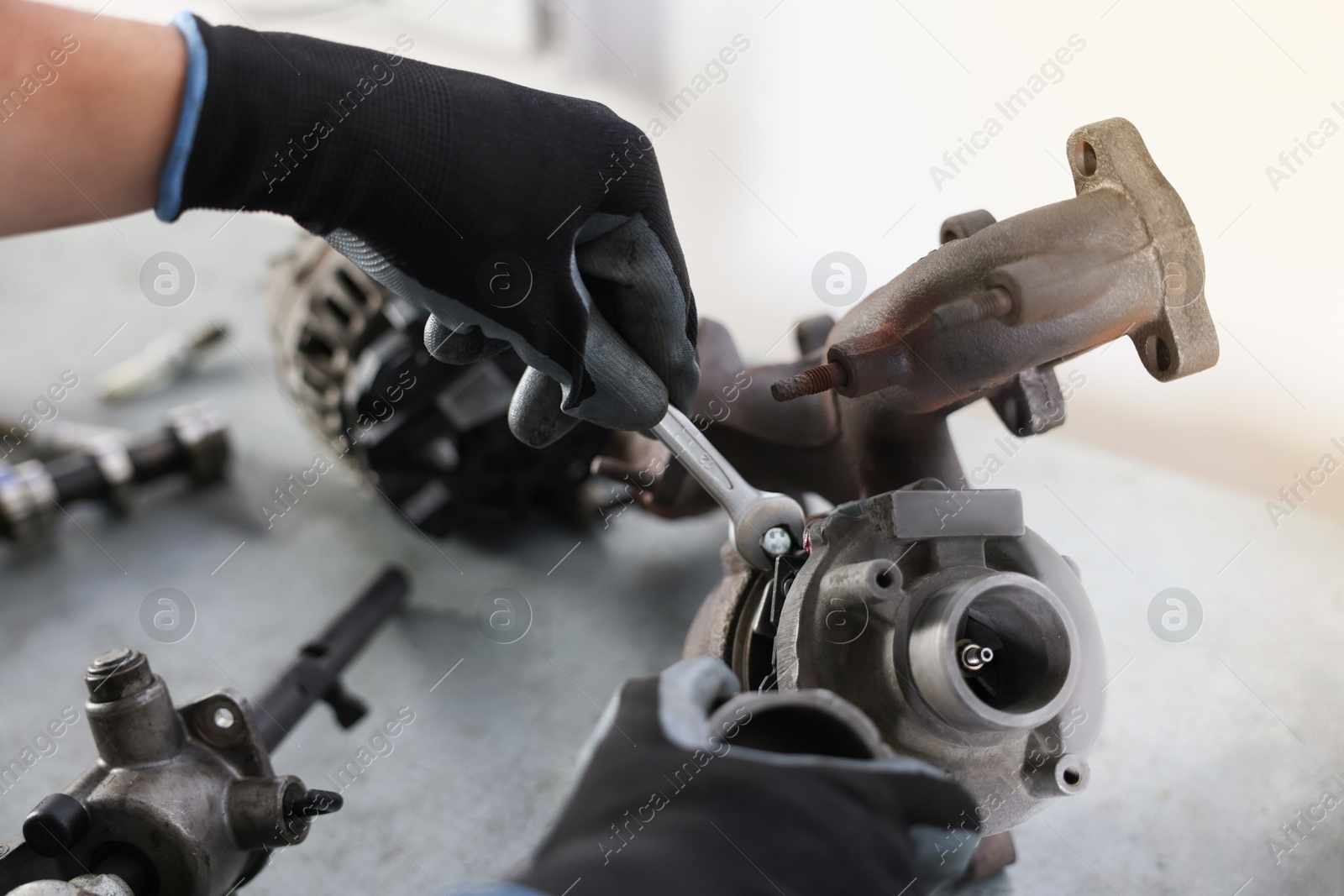 Auto parts. Professional mechanic with wrench fixing turbocharger at grey table indoors, closeup Photo of Auto parts. Professional mechanic with wrench fixing turbocharger at grey table indoors, closeup