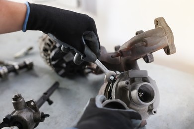Photo of Auto parts. Professional mechanic with wrench fixing turbocharger at grey table indoors, closeup