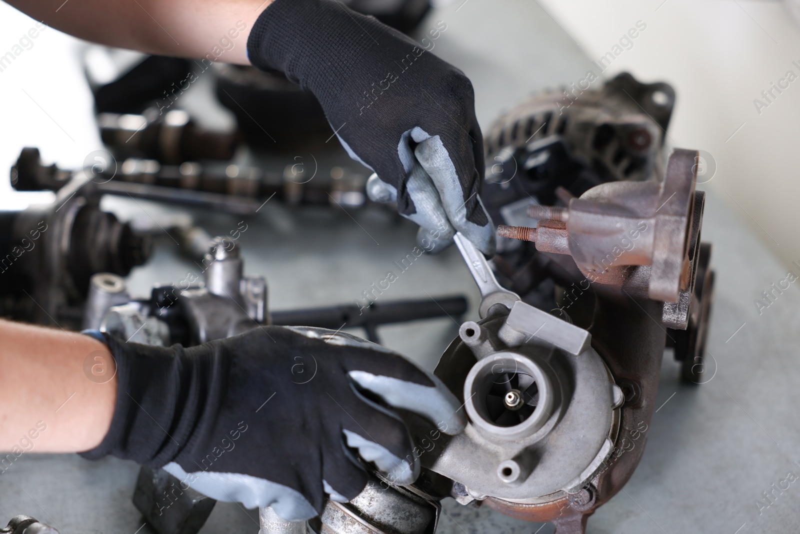 Auto parts. Professional mechanic with wrench fixing turbocharger at grey table indoors, above view Photo of Auto parts. Professional mechanic with wrench fixing turbocharger at grey table indoors, above view