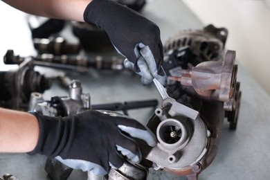 Photo of Auto parts. Professional mechanic with wrench fixing turbocharger at grey table indoors, above view