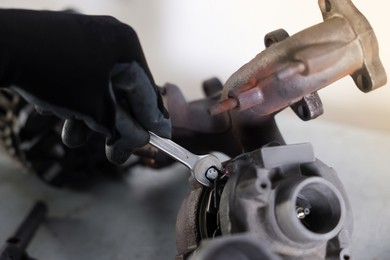 Photo of Auto parts. Professional mechanic with wrench fixing turbocharger at grey table indoors, closeup