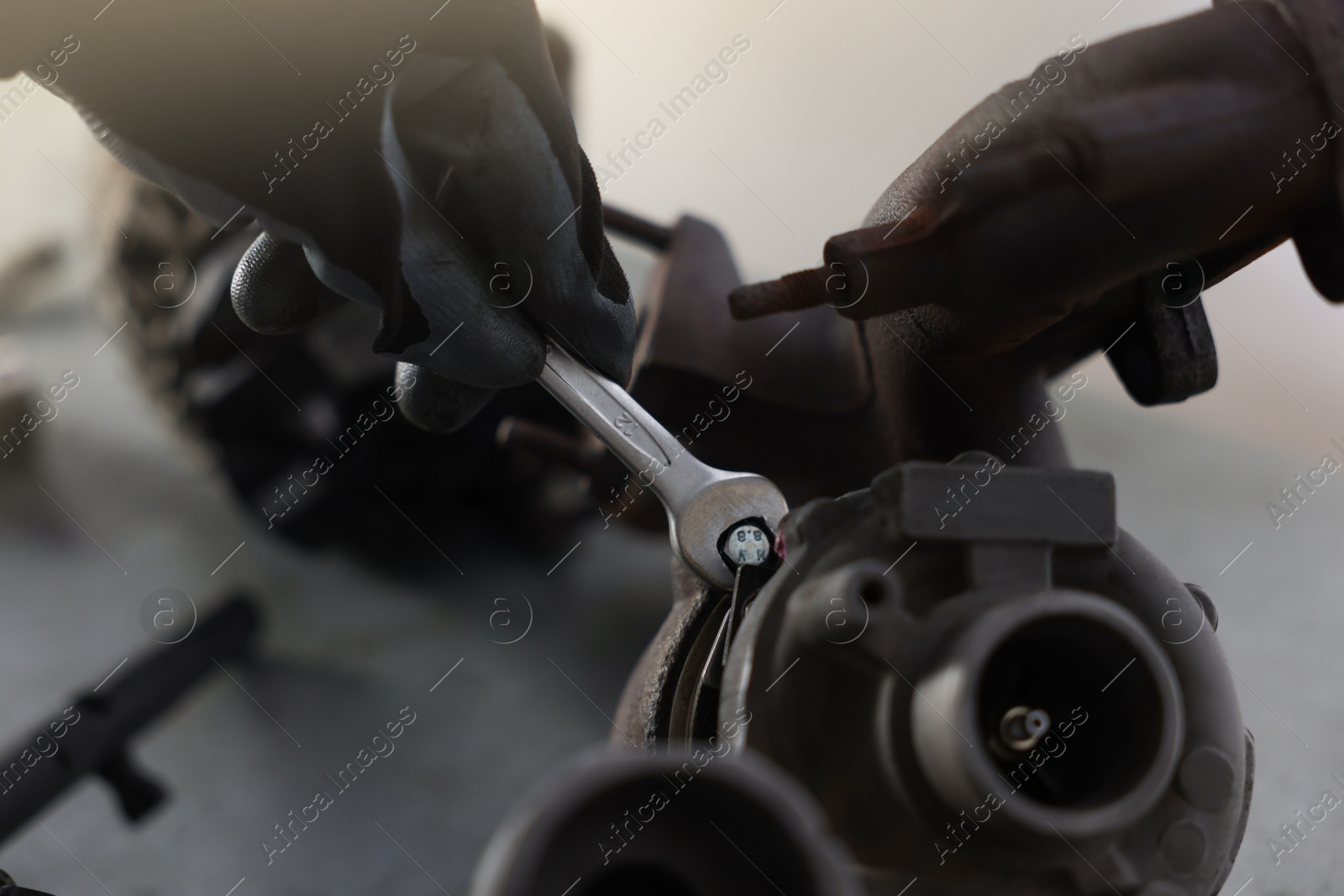 Auto parts. Professional mechanic with wrench fixing turbocharger at grey table indoors, closeup Photo of Auto parts. Professional mechanic with wrench fixing turbocharger at grey table indoors, closeup