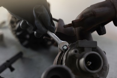 Photo of Auto parts. Professional mechanic with wrench fixing turbocharger at grey table indoors, closeup