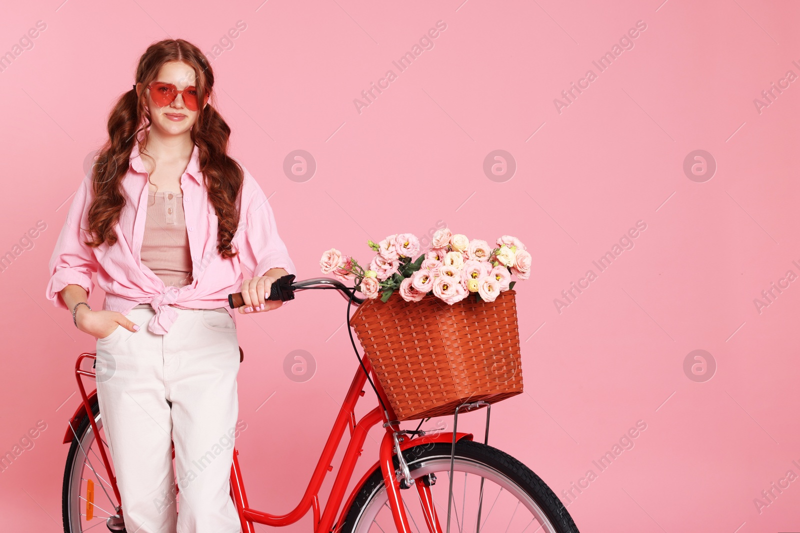 Beautiful teenage girl in sunglasses and bicycle with basket of flowers against pink background. Space for text Photo of Beautiful teenage girl in sunglasses and bicycle with basket of flowers against pink background. Space for text