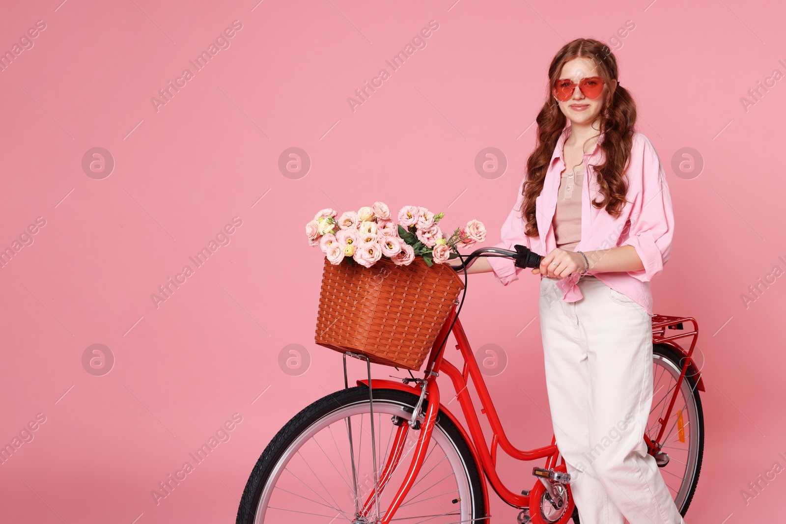 Beautiful teenage girl in sunglasses and bicycle with basket of flowers against pink background. Space for text Photo of Beautiful teenage girl in sunglasses and bicycle with basket of flowers against pink background. Space for text
