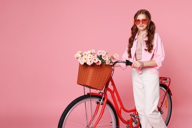 Photo of Beautiful teenage girl in sunglasses and bicycle with basket of flowers against pink background. Space for text