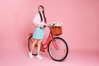 Photo of Smiling woman and bicycle with basket of flowers against pink background