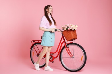 Photo of Smiling woman and bicycle with basket of flowers against pink background