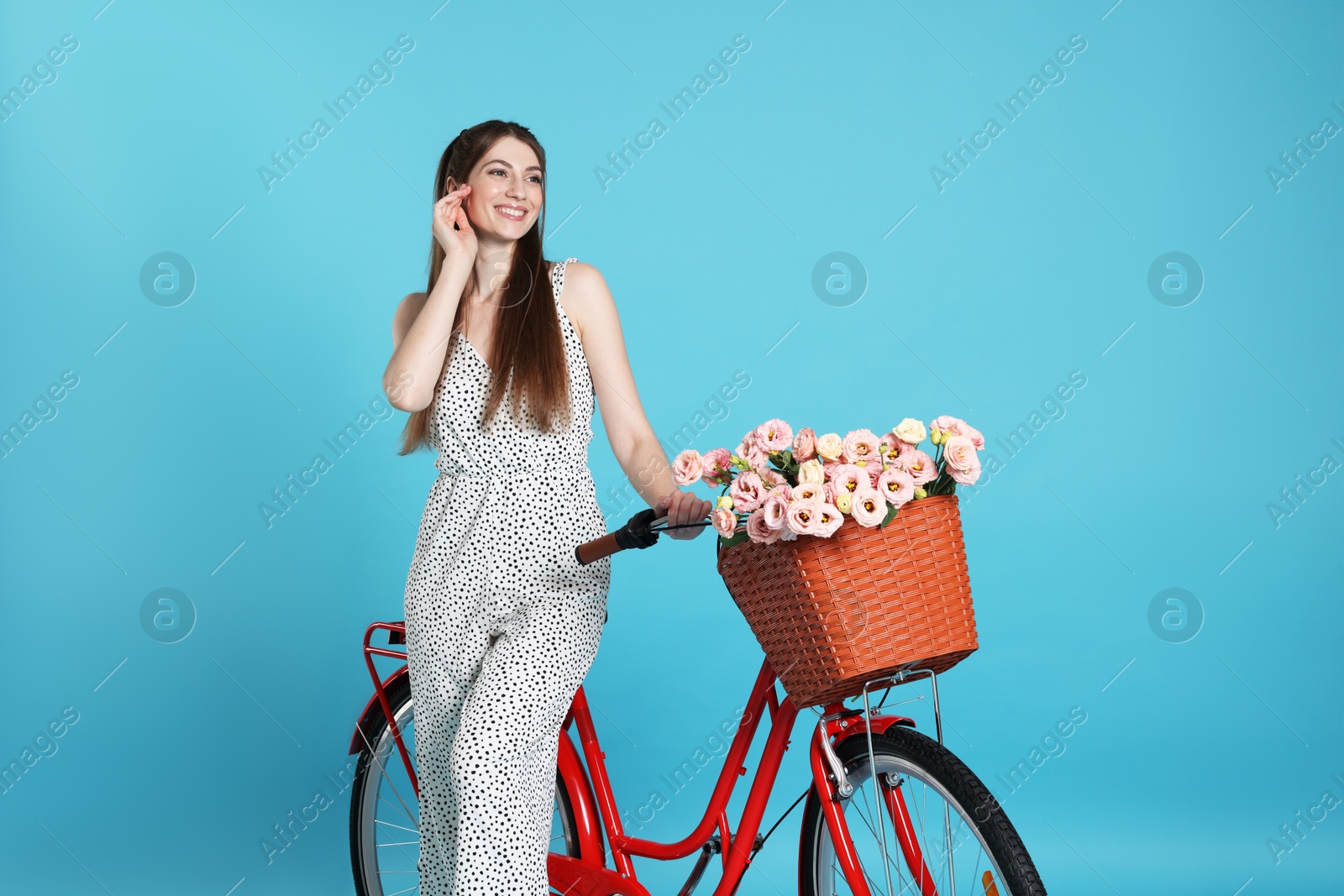 Smiling woman and bicycle with basket of flowers against light blue background Photo of Smiling woman and bicycle with basket of flowers against light blue background