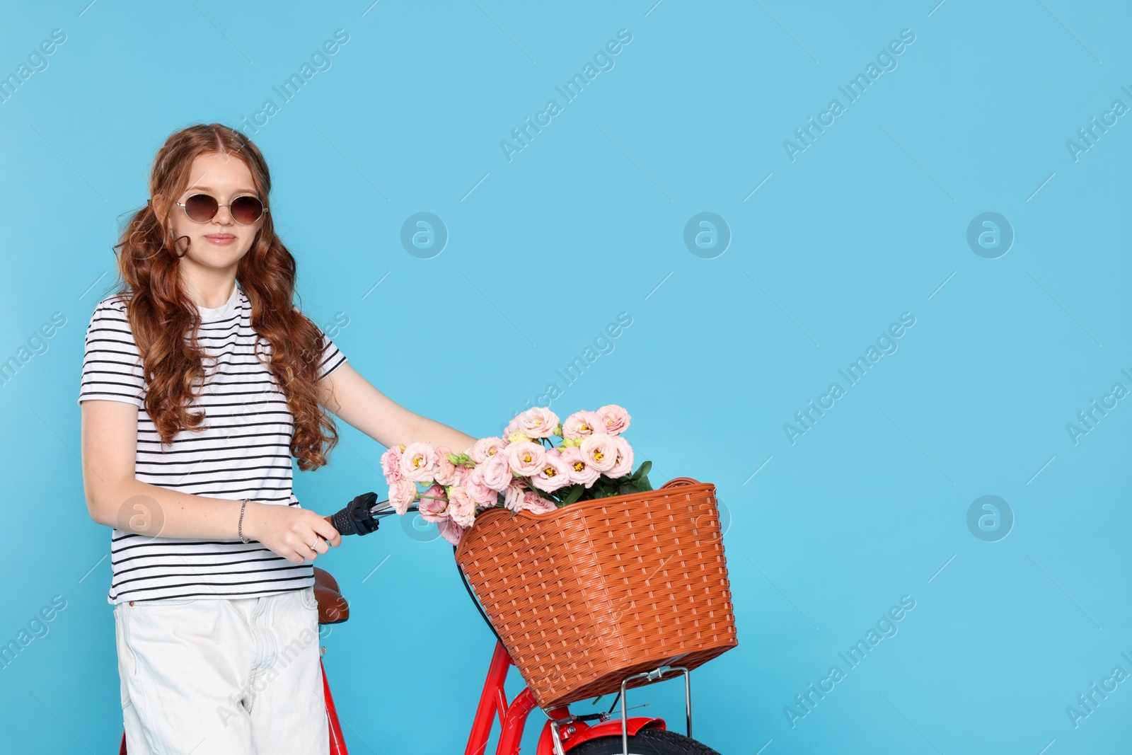 Beautiful teenage girl in sunglasses and bicycle with basket of flowers against light blue background. Space for text Photo of Beautiful teenage girl in sunglasses and bicycle with basket of flowers against light blue background. Space for text
