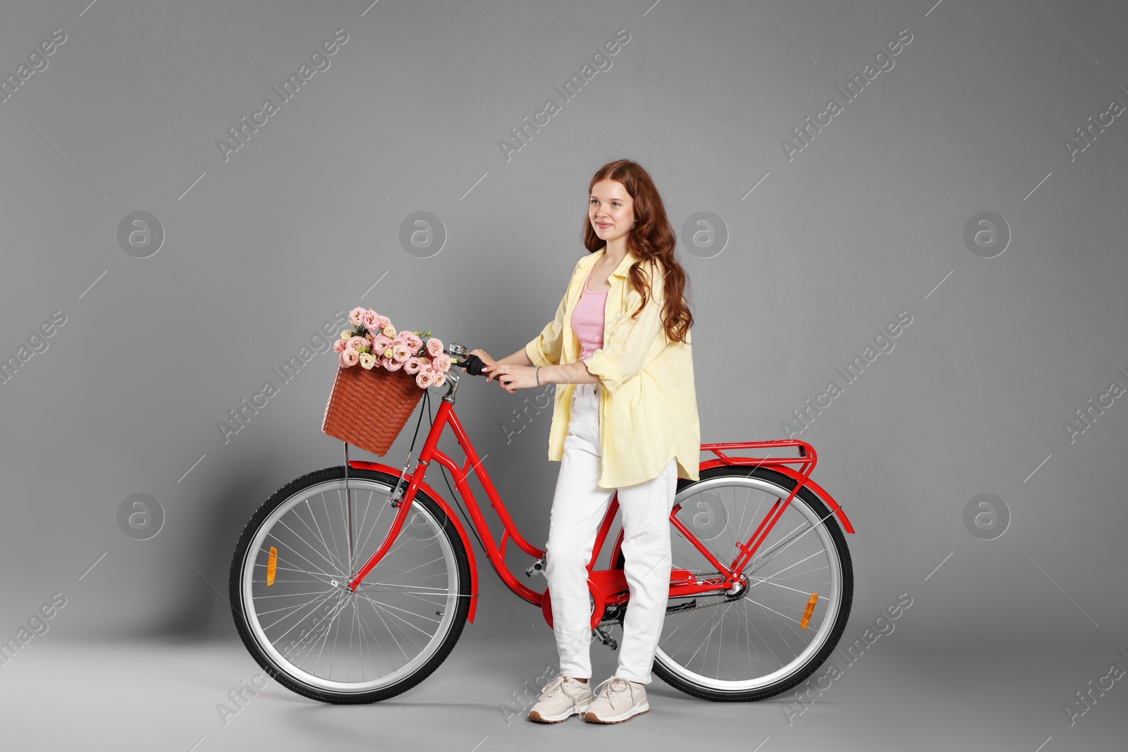 Beautiful teenage girl and bicycle with basket of flowers against grey background Photo of Beautiful teenage girl and bicycle with basket of flowers against grey background