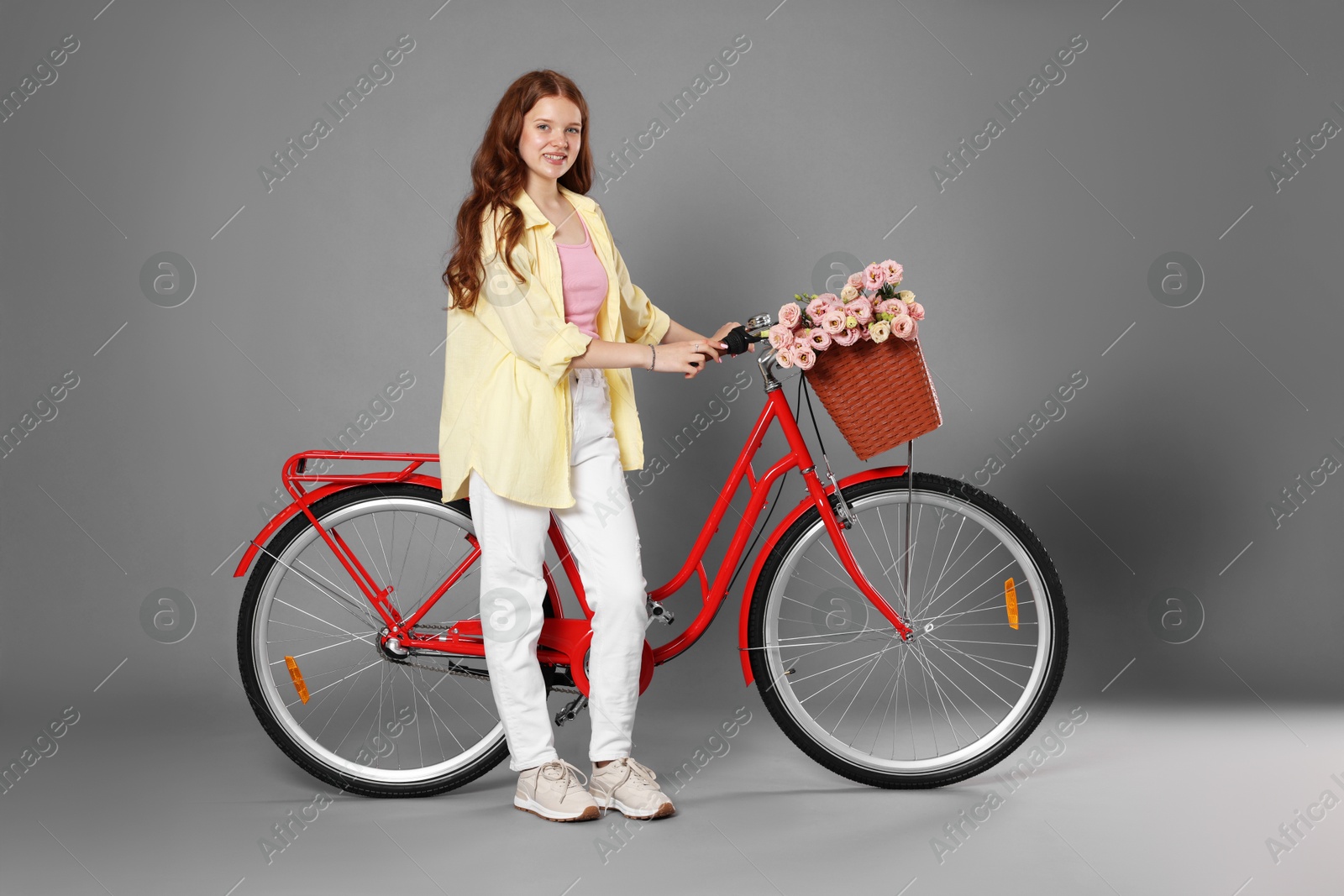 Photo of Smiling teenage girl and bicycle with basket of flowers against grey background