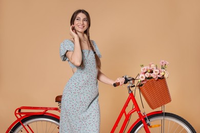 Photo of Smiling woman in dress and bicycle with basket of flowers on beige background