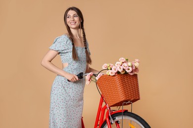 Photo of Smiling woman in dress and bicycle with basket of flowers on beige background