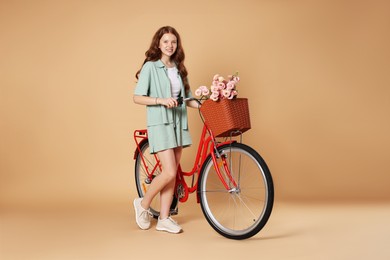 Photo of Smiling teenage girl and bicycle with basket of flowers against beige background
