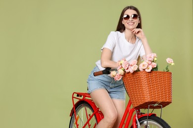 Photo of Smiling woman in sunglasses posing on bicycle with basket of flowers against green background. Space for text