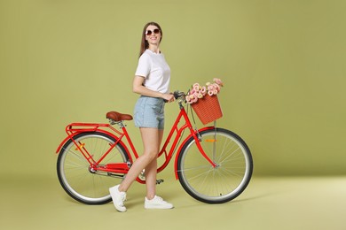 Photo of Smiling woman in sunglasses and bicycle with basket of flowers on green background