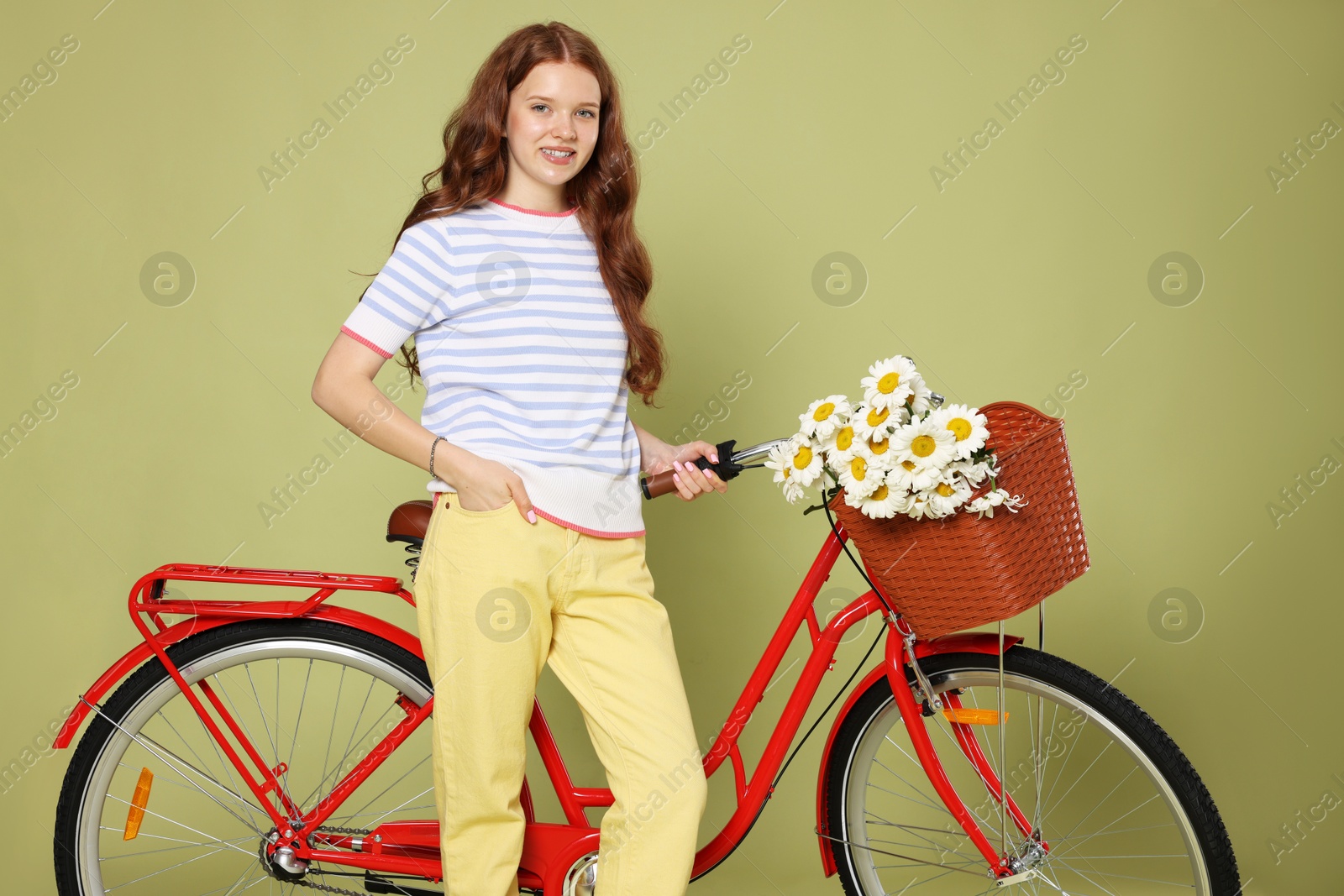 Smiling teenage girl and bicycle with basket of flowers against green background Photo of Smiling teenage girl and bicycle with basket of flowers against green background
