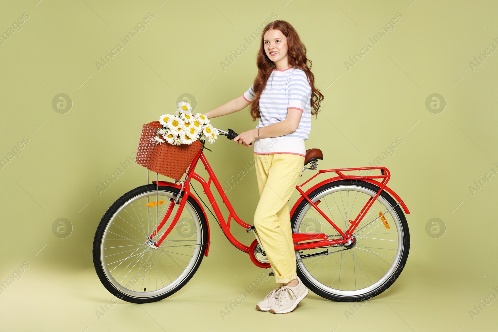 Photo of Smiling teenage girl and bicycle with basket of flowers against green background