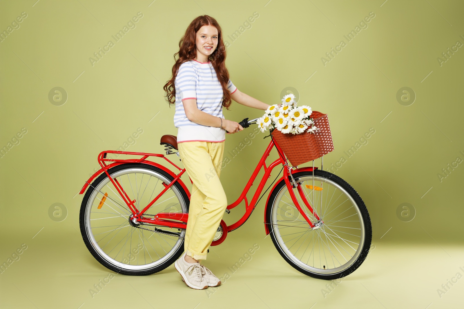 Photo of Smiling teenage girl and bicycle with basket of flowers against green background
