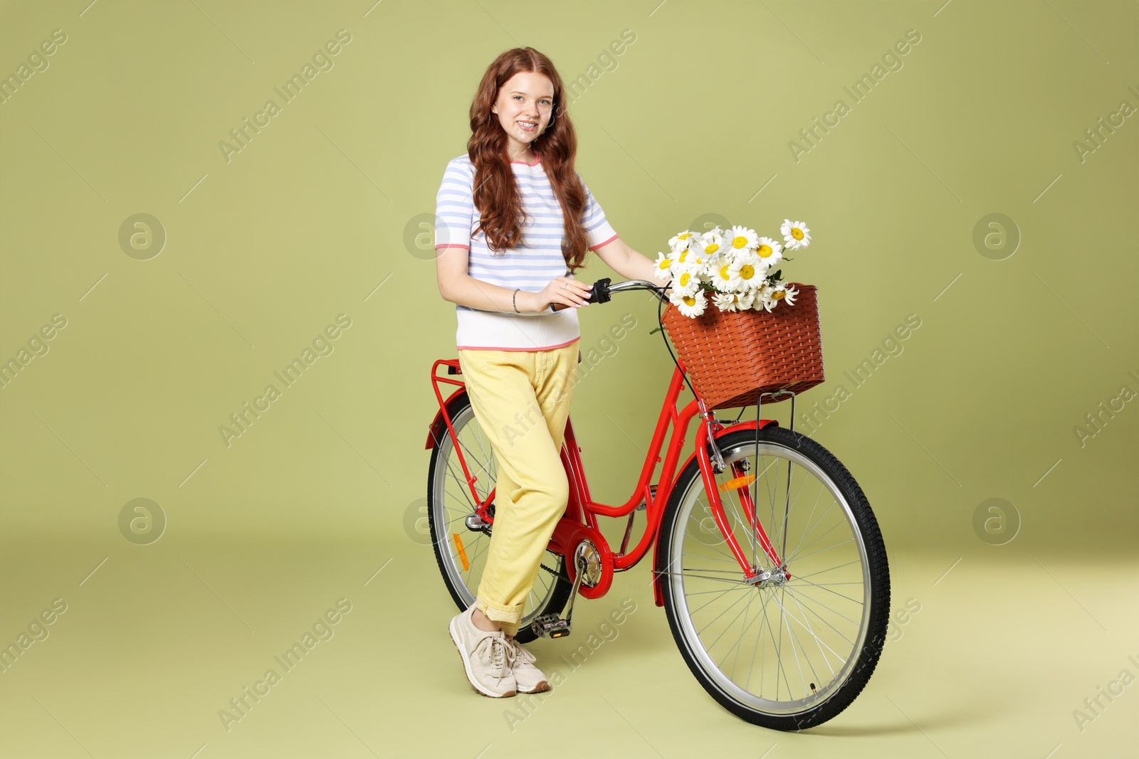 Smiling teenage girl and bicycle with basket of flowers against green background Photo of Smiling teenage girl and bicycle with basket of flowers against green background