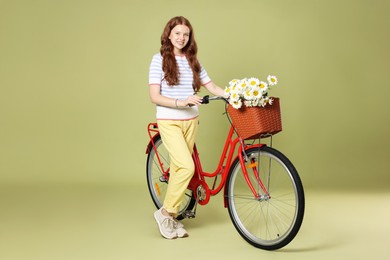 Photo of Smiling teenage girl and bicycle with basket of flowers against green background