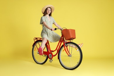 Photo of Smiling woman in hat riding bicycle with basket against light green background