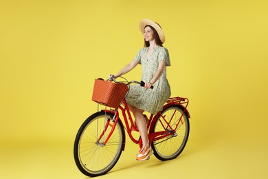 Photo of Smiling woman in hat riding bicycle with basket against light green background