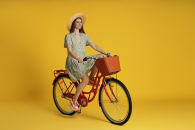 Photo of Smiling woman in hat riding bicycle with basket against yellow background