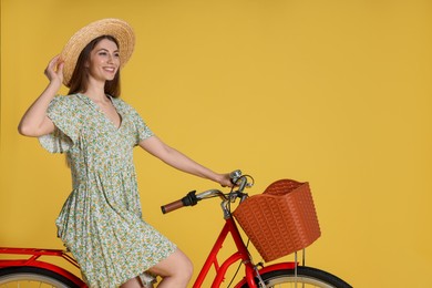 Photo of Smiling woman in hat riding bicycle with basket against yellow background. Space for text