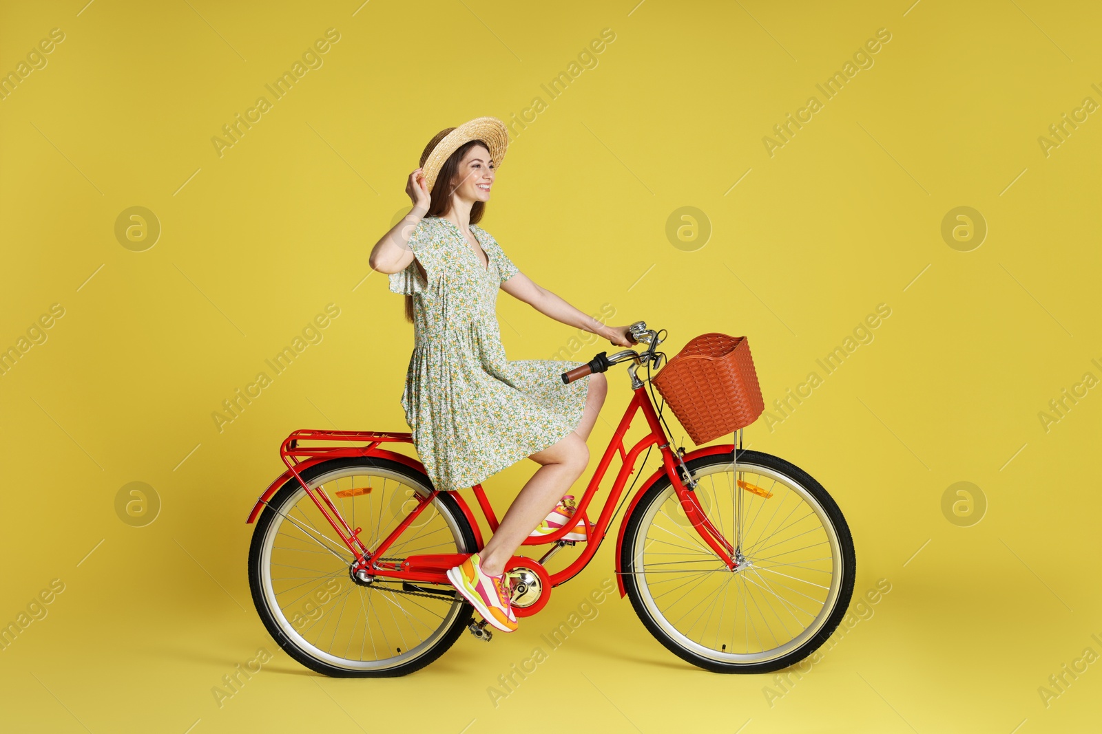 Photo of Smiling woman in hat riding bicycle with basket against light green background