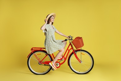 Photo of Smiling woman in hat riding bicycle with basket against light green background