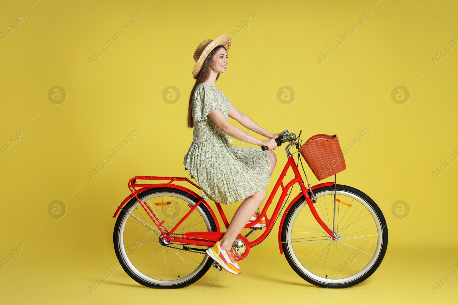 Smiling woman in hat riding bicycle with basket against light green background Photo of Smiling woman in hat riding bicycle with basket against light green background