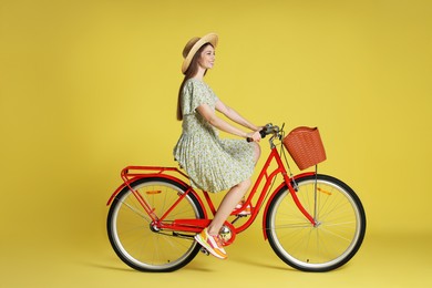Photo of Smiling woman in hat riding bicycle with basket against light green background