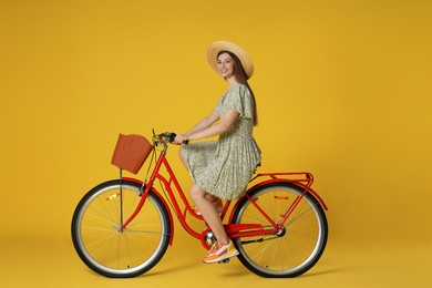 Photo of Smiling woman in hat riding bicycle with basket against yellow background